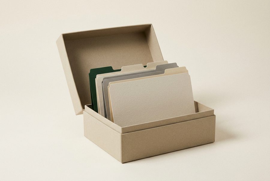 Una caja de archivo abierta con una hilera de separadores en blanco, alineados con precisión y una pestaña en verde oscuro.